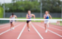 3 runners in soft focus on a track running towards the finish line