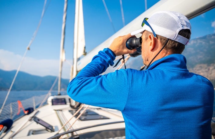 Young man captain on the yacht looking through binoculars during sailing boat control. Travel and active life.