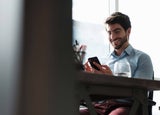 Man sitting at a desk, looking at his smartphone and smiling